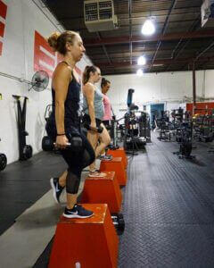 Women performing a farmer’s carry exercise with dumbbells during a functional strength training class at Elite Edge Fitness in Chamblee, Georgia